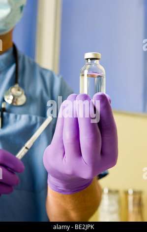 Maschio di medico o infermiere indossando blue scrubs, uno stetoscopio e guanti mantiene la fiala di sostanza farmaceutica e la siringa. Foto Stock