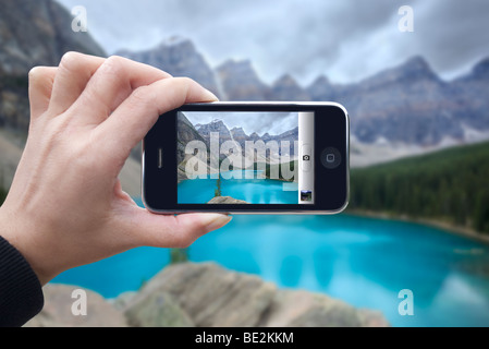 Turista femminile tenere per mano le persone il suo iphone 3Gs tenendo foto del Lago Moraine in Alberta, Canada Foto Stock