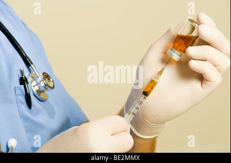 Maschio di medico o infermiere indossando blue scrubs, uno stetoscopio e guanti mantiene la fiala di sostanza farmaceutica e la siringa. Foto Stock