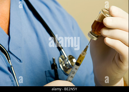 Maschio di medico o infermiere indossando blue scrubs, uno stetoscopio e guanti mantiene la fiala di sostanza farmaceutica e la siringa. Foto Stock