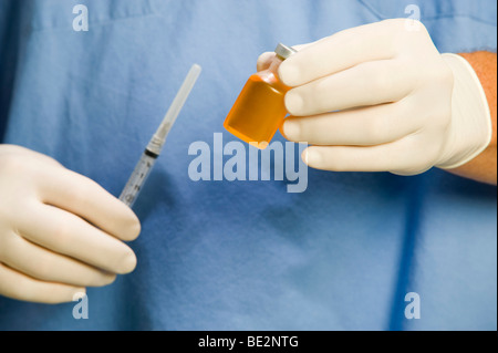 Maschio di medico o infermiere indossando blue scrubs, uno stetoscopio e guanti mantiene la fiala di sostanza farmaceutica e la siringa. Foto Stock