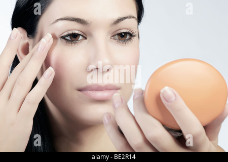 Giovane donna applicando eye shadow mentre cercano in un piccolo specchio per il trucco e la bellezza Foto Stock