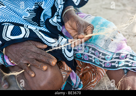 Una vecchia donna che produce una corda di una noce di cocco il guscio, Jambiani, Zanzibar, Tanzania Africa Foto Stock