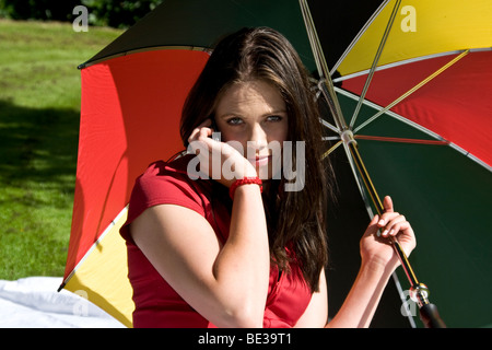 Donna riparo dal sole sotto un brolly durante la conversazione su un telefono cellulare all'interno del Giardino Botanico di Dundee, Regno Unito Foto Stock