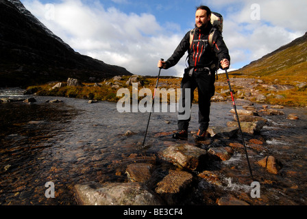 Escursionista con zaino da trekking ed escursionismo poli sul sentiero di montagna di fronte ad un picco innevato, Liathach, Torridon, Scozia, Regno Ki Foto Stock