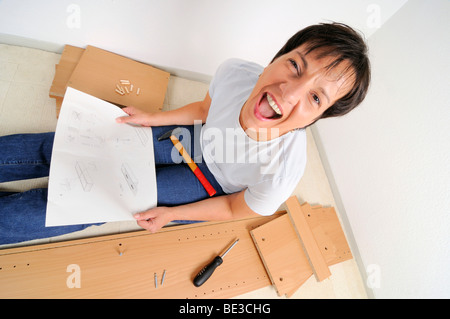 Frustrati donna assemblaggio di mobili e urlando, leggere le istruzioni Foto Stock