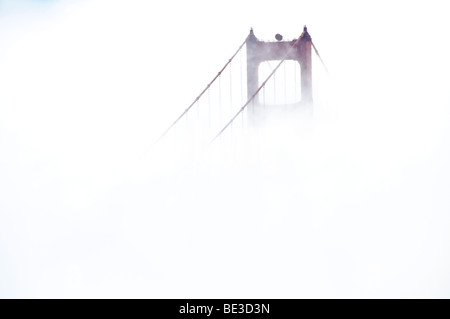 Golden Gate Bridge Tower a Fog San Francisco California USA // SAN FRANCISCO, California - Una torre del Golden Gate Bridge, un ponte sospeso, è parzialmente oscurata dalla nebbia sulla baia di San Francisco. Completato nel 1937, il ponte è riconosciuto per il suo caratteristico design Art Deco. Collega la città di San Francisco alla contea di Marin, attraversando lo stretto del Golden Gate. La sua costruzione fu un notevole risultato ingegneristico, superando condizioni difficili. Il colore International Orange del ponte è stato scelto per migliorare la sua visibilità in condizioni di nebbia. Foto Stock