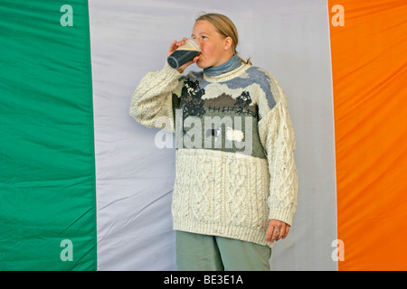 Ritratto di una giovane donna di bere una pinta di Guinness davanti alla bandiera irlandese Foto Stock