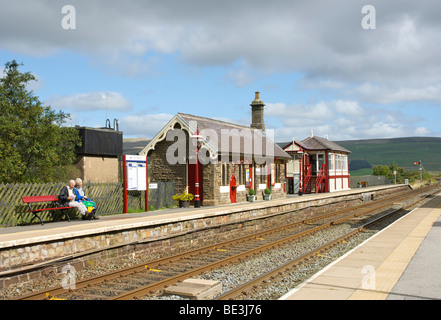 Giovane seduto su un banco di lavoro, Garsdale stazione, sul Settle-Carlisle linea ferroviaria, Yorkshire Dales National Park, England Regno Unito Foto Stock