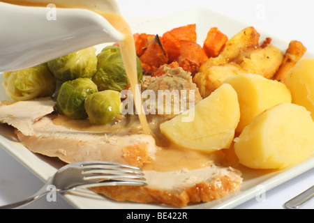 Versando il sugo di carne su una festosa turchia pasto, con patate arrosto e un arrosto di pastinaca, patate bollite e ripieno Foto Stock