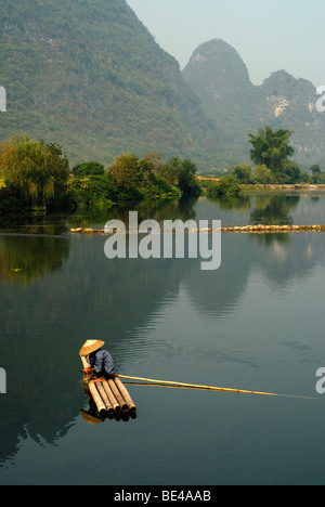 Pescatore cinese con un cappello di paglia su una zattera di bamboo la pesca vicino a Yangshuo nel fiume Yulong davanti a scogliere calcaree, Yan Foto Stock