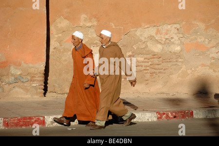 Gli uomini marocchini indossando il tradizionale Jellaba mantelli & Skull Caps camminare oltre le mura della città di Marrakech marocco Foto Stock