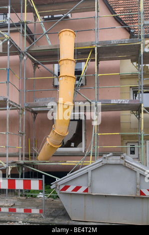 Casa Scaffolded con annesso scivolo dei detriti, i contenitori della spazzatura e marcature di sicurezza Foto Stock