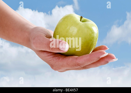 Mano che tiene una mela verde contro un cielo blu Foto Stock