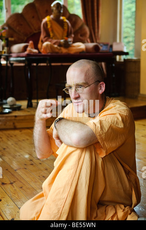 Hare Krishna discepolo in una stanza del tempio con statua della Sua Divina Grazia A.C. Bhaktivedanta Swami Prabhupada dietro. Foto Stock