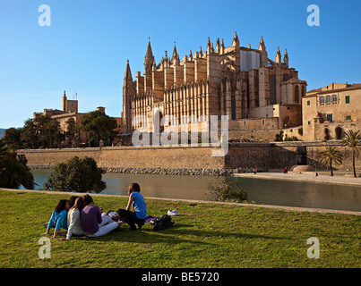 Un gruppo di bambini seduti su erba con la cattedrale di Palma Mallorca Spagna Spain Foto Stock