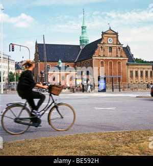 Una giovane donna in sella ad una bicicletta con un cestino in estate passato Borsgade edificio in Copenhagen DANIMARCA KATHY DEWITT Foto Stock