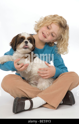 A sette anni di ragazza con il suo Shih Tzu cane, sorridente e guardando il visualizzatore. Foto Stock