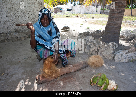 Una vecchia donna che produce una corda di una noce di cocco il guscio, Jambiani, Zanzibar, Tanzania Africa Foto Stock