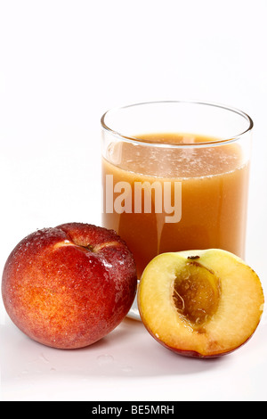 Bicchiere di succo di pesca dietro due pesche, uno dimezzato Foto Stock