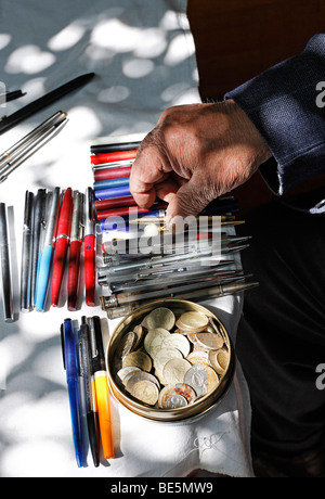 La mano di un uomo vecchio di smistamento utilizzato biros su un tavolo, monete in barattolo di latta, prenota bazaar, Beyazit Square, Istanbul, Turchia Foto Stock