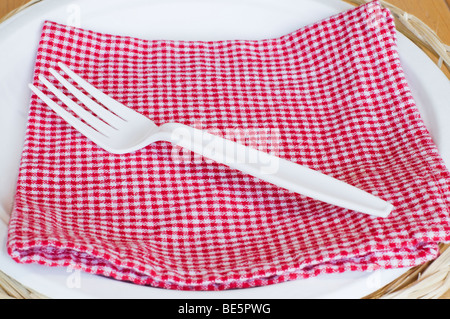 Luogo pic-nic impostazione con un bianco forcella di plastica, rosso controllato e tovagliolo di carta bianco piastra. Foto Stock