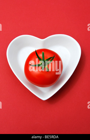 Singola vite il pomodoro in un cuore a forma di tazza di porcellana Foto Stock