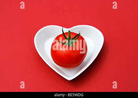 Singola vite il pomodoro in un cuore a forma di tazza di porcellana Foto Stock