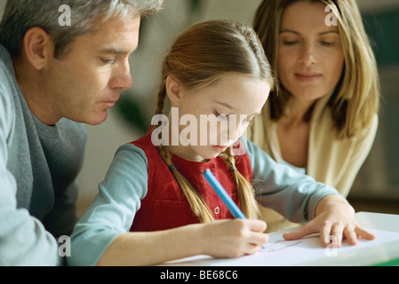 Bambina disegno, i genitori seduti su entrambi i lati, a guardare oltre la sua spalla Foto Stock