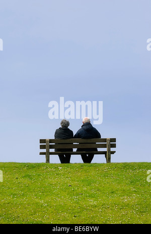 Coppia di anziani seduti su una panchina su una diga Foto Stock