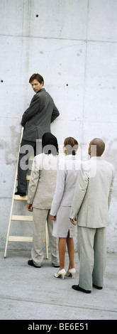 Imprenditore scaletta di arrampicata, guardando sopra la spalla a professionisti allineati dietro di lui Foto Stock