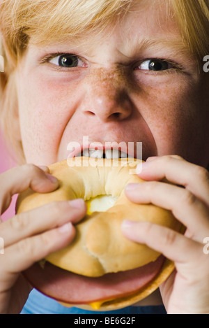 Ragazzo di mordere in prosciutto e formaggio bagel sandwich, close-up Foto Stock