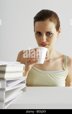 Donna prendendo break, bere dalla tazza monouso, stack di leganti in primo piano Foto Stock