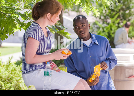 Interacial giovane, (African American teen maschio e caucasici ragazza adolescente)sedere fuori e mangiare il pranzo e spuntini salutari Foto Stock