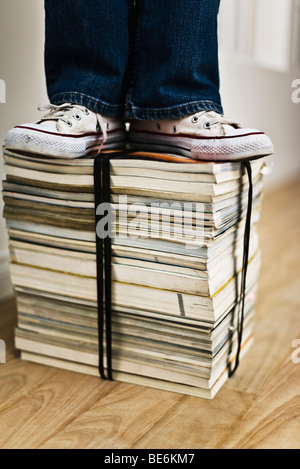 Persona in piedi sulla parte superiore della pila di legato di libri e riviste Foto Stock
