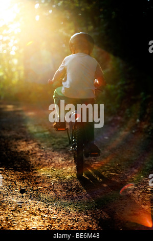 Bambino ragazzo in bicicletta attraverso una foresta corsa in bicicletta con il casco protettivo Foto Stock