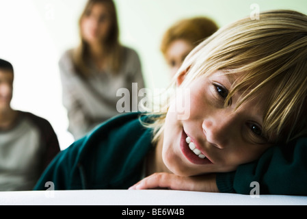 Ragazzo appoggiato la testa sulle braccia, sorridente in telecamera Foto Stock