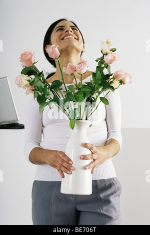 Donna che mantiene un vaso di rose, sorridente con testa indietro Foto Stock