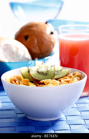 La prima colazione, cornflakes con fette di kiwi, succo d'arancia e rotoli Foto Stock