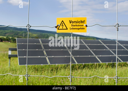 Il fotovoltaico, moduli diretto su diversi supporti o cremagliere dietro il recinto di protezione con il pericolo della lettura del segno Starkstro Vorsicht Foto Stock