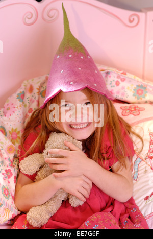 Bambina cuddling con il suo giocattolo e indossa un cappello spiritoso, della ragazza sogno rosa Foto Stock