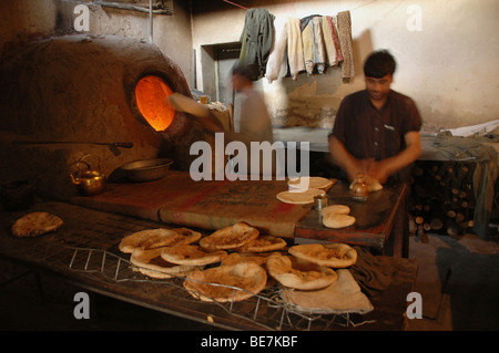 Due giovani uomini la cottura del pane in un tradizionale forno di argilla in un panificio della capitale afgana di Kabul, Afghanistan Foto Stock