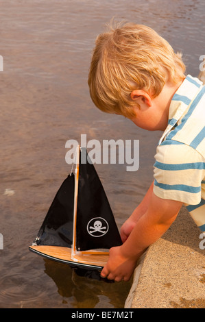 Un piccolo ragazzo ( il modello rilasciato ) vela il suo giocattolo in barca il lago in barca in Aldeburgh , Suffolk , Regno Unito Foto Stock