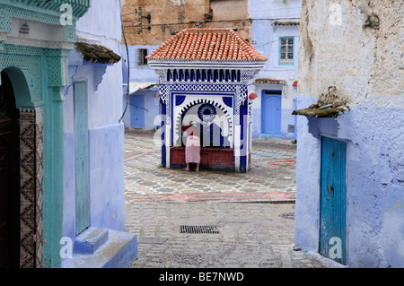 Il Marocco; Chefchaouen; Scene di strada nella Medina che mostra una donna ad una delle pubbliche fontane di acqua Foto Stock