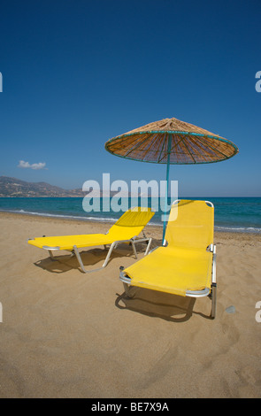 Giallo due lettini e ombrelloni di paglia sulla deserta spiaggia sabbiosa con cielo blu e distante piccola nube bianca Foto Stock