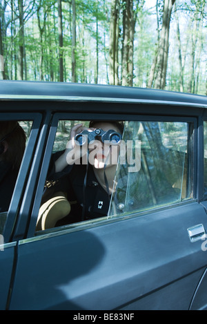 Donna seduta in auto, a guardare fuori dalla finestra attraverso il binocolo Foto Stock