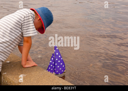 Un piccolo ragazzo ( il modello rilasciato ) vela il suo giocattolo in barca il lago in barca in Aldeburgh , Suffolk , Regno Unito Foto Stock