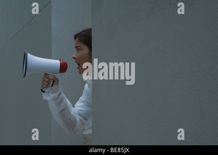 Donna in tuta protettiva urlando nel megafono, vista laterale Foto Stock