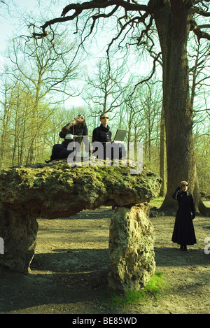 Due persone sedute sulla formazione di roccia con lampada, tramite telefono, computer portatile, donna in piedi in background Foto Stock