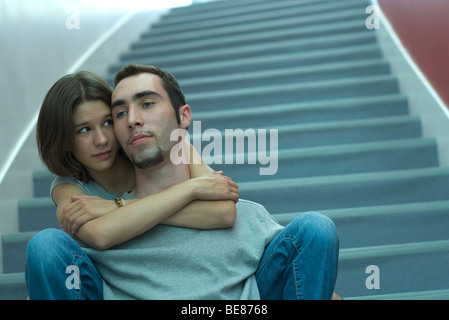 Coppia giovane seduti insieme su scale, abbracciando femmina maschio da dietro Foto Stock